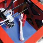 A bright red 3D printing machine is shown rendering a canine limb model.