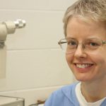 Kim Sherman is shown sitting in exam room with eye exam equipment next to her.