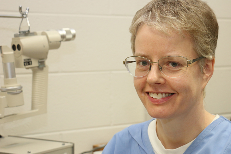 Kim Sherman is shown sitting in exam room with eye exam equipment next to her.