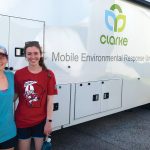 Two women students stand in front of a mobile environmental response unit van.