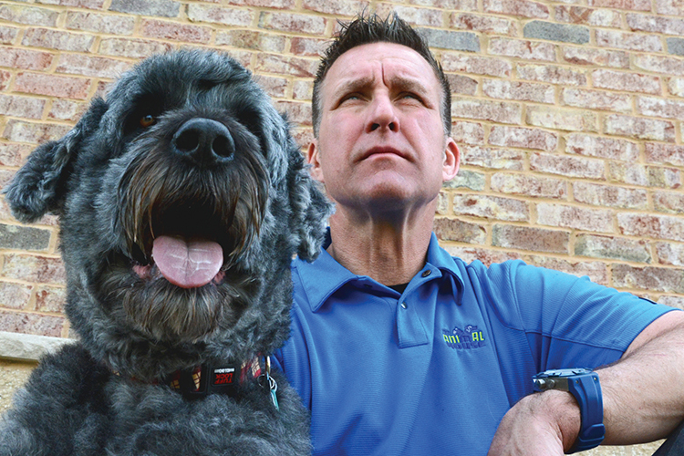 Man in blue shirt sits with his big black dog.