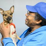 Man in blue baseball cap adoringly holds his little dog