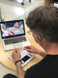 Clinical professor Robert Hardie demonstrates surgical knot tying while a student, seen on the laptop, practices the same suturing skills remotely and receives real-time feedback