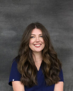 A long brown wavy hair woman wearing a navy scrub top. Caitlin Eliason