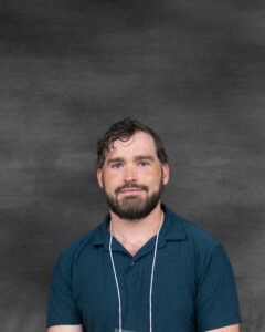 A short wavy brown hair man with a beard wearing a teal blue polo shirt. Chip Clark