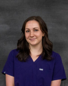 A long dark brown hair woman wearing a navy scrub top. Evelyn Patient