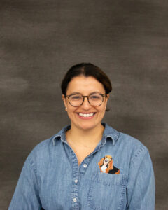 A dark brown pulled back hair woman wearing a denim long sleeve button shirt with a beagle embroidery design on left chest. Jennifer Zamora