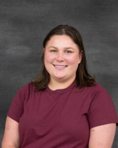 A medium length brown hair woman wearing a short sleeve burgundy shirt. Linley Cook