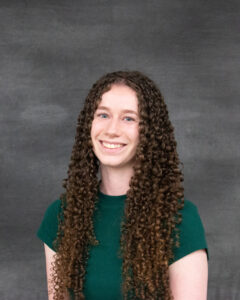 A long curly brown hair woman wearing a green short sleeve top. Megan Brobst