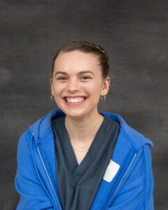 A woman with pulled back brown hair wearing a scrub blue top with light blue sweatshirt. Nicole Moyer
