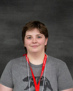 A brown short hair person wearing gray tshirt and nametag lanyard. Olivia Allen